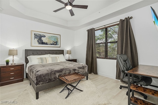 bedroom featuring ceiling fan, light wood-type flooring, and a tray ceiling