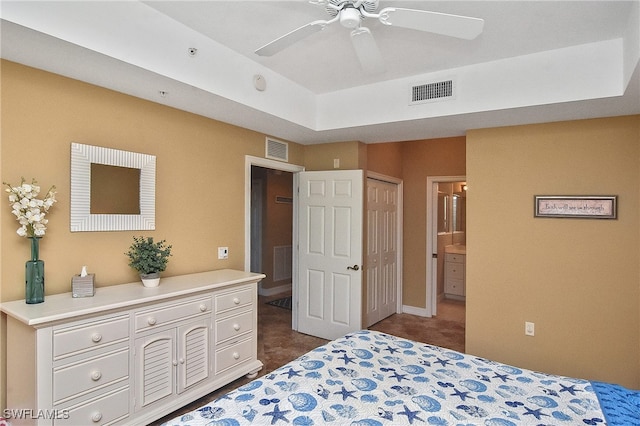 bedroom featuring a tray ceiling, connected bathroom, dark carpet, and ceiling fan