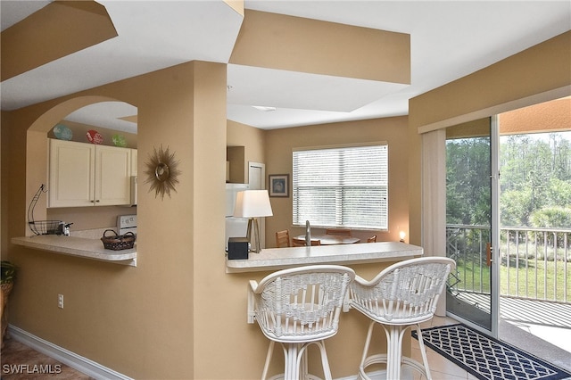 kitchen featuring kitchen peninsula, light tile patterned flooring, and a breakfast bar area