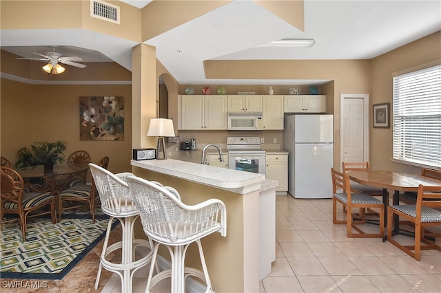 kitchen with a breakfast bar, white appliances, kitchen peninsula, light tile patterned floors, and ceiling fan