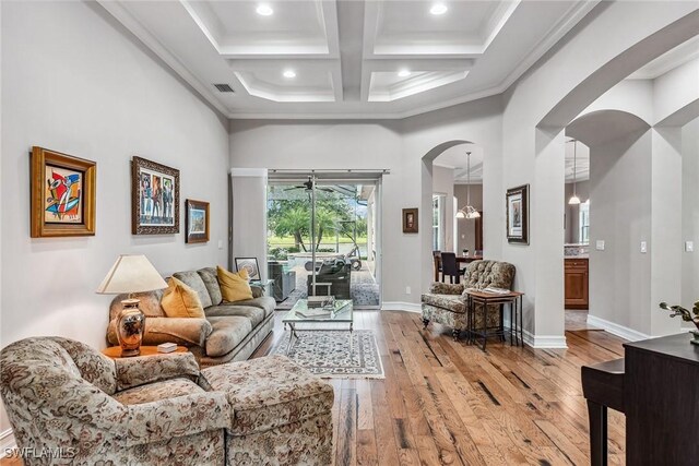 living room featuring coffered ceiling, light wood-type flooring, crown molding, and a towering ceiling