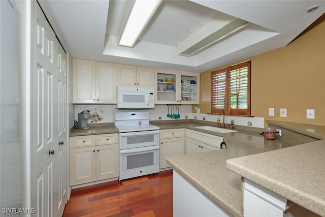 kitchen with wood-type flooring, sink, kitchen peninsula, white appliances, and a raised ceiling