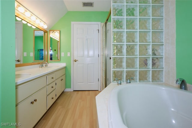 bathroom featuring vanity, tiled bath, vaulted ceiling, and hardwood / wood-style flooring