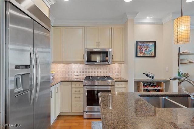 kitchen with sink, cream cabinetry, hanging light fixtures, and high end appliances