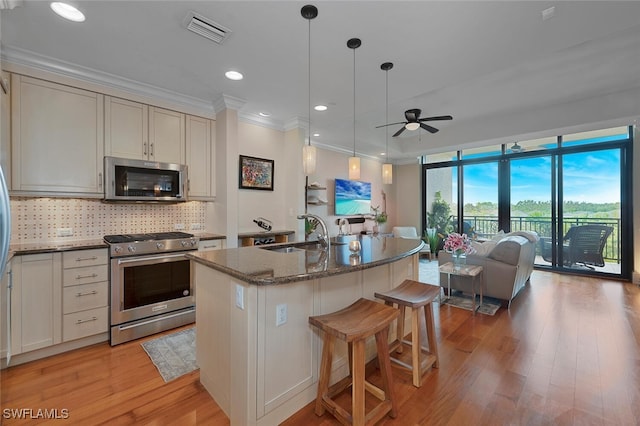 kitchen featuring a kitchen island with sink, sink, ceiling fan, stone countertops, and stainless steel appliances