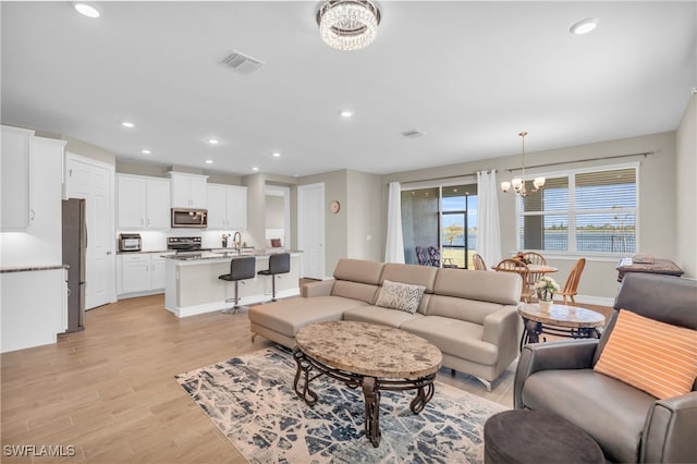 living room featuring sink, light hardwood / wood-style flooring, and an inviting chandelier