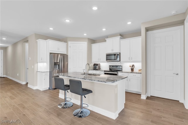 kitchen featuring light hardwood / wood-style flooring, an island with sink, white cabinetry, appliances with stainless steel finishes, and light stone counters