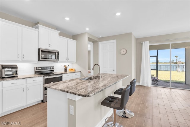 kitchen with sink, appliances with stainless steel finishes, light hardwood / wood-style floors, and an island with sink