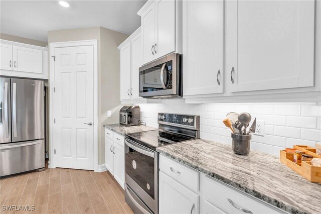 kitchen with decorative backsplash, light wood-type flooring, white cabinetry, appliances with stainless steel finishes, and light stone counters