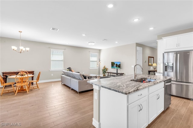 kitchen with stainless steel appliances, a center island with sink, sink, white cabinetry, and light hardwood / wood-style floors