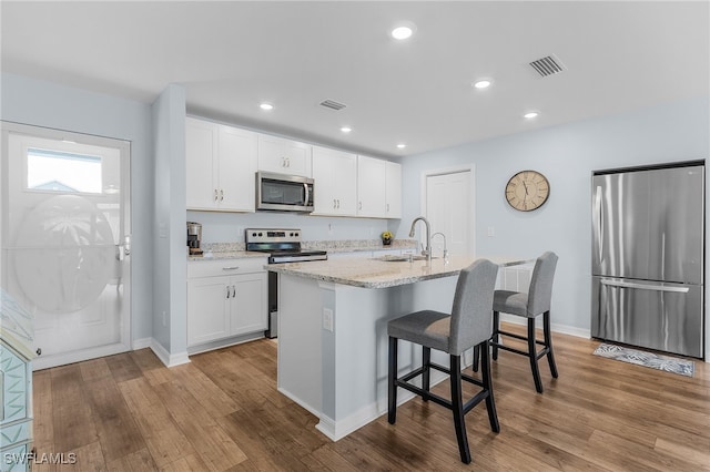 kitchen featuring an island with sink, light wood-type flooring, white cabinetry, and appliances with stainless steel finishes