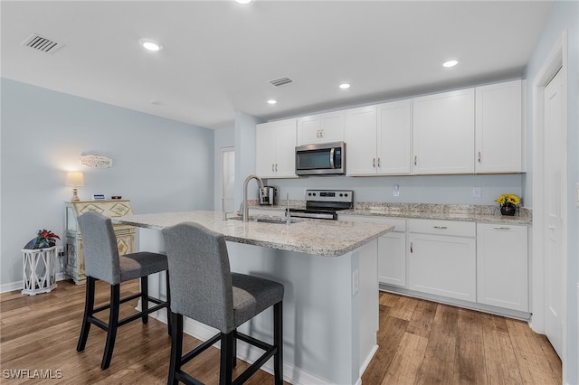 kitchen with an island with sink, stainless steel appliances, white cabinets, and light hardwood / wood-style floors