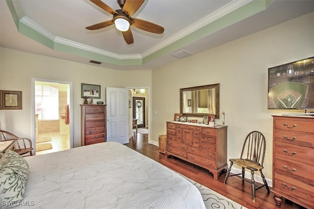 bedroom featuring dark wood-type flooring, a raised ceiling, crown molding, ceiling fan, and ensuite bathroom