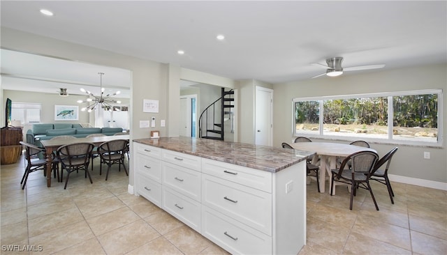 kitchen featuring light tile patterned flooring, dark stone counters, white cabinetry, a center island, and ceiling fan with notable chandelier