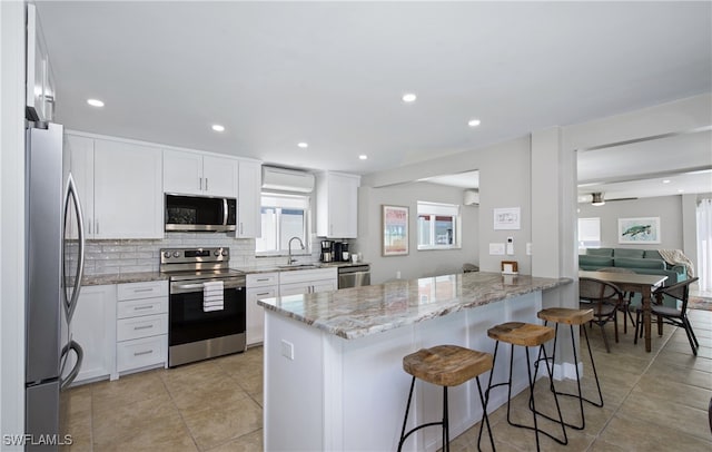 kitchen with ceiling fan, light stone counters, white cabinetry, appliances with stainless steel finishes, and a breakfast bar