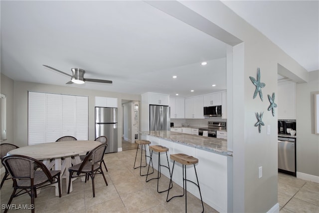 kitchen with light stone counters, white cabinets, decorative backsplash, stainless steel appliances, and ceiling fan