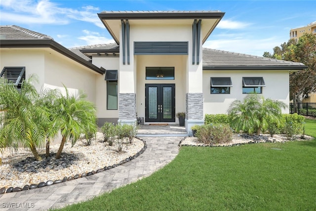 property entrance featuring a yard, french doors, stone siding, a tiled roof, and stucco siding