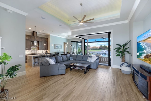 living area featuring ceiling fan, visible vents, baseboards, light wood-type flooring, and a tray ceiling