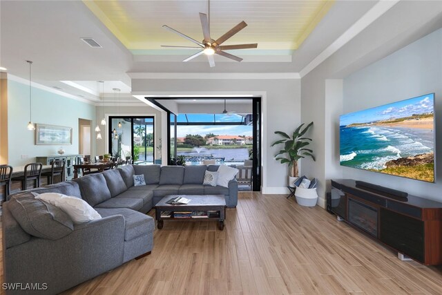 living room featuring ceiling fan, a raised ceiling, crown molding, and light hardwood / wood-style flooring