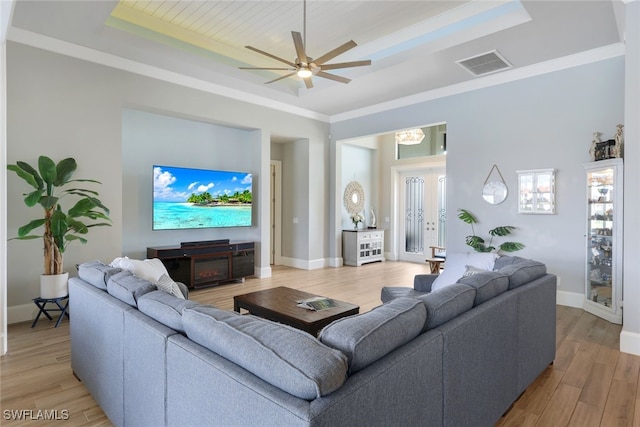 living area with a raised ceiling, visible vents, light wood-style floors, ornamental molding, and baseboards