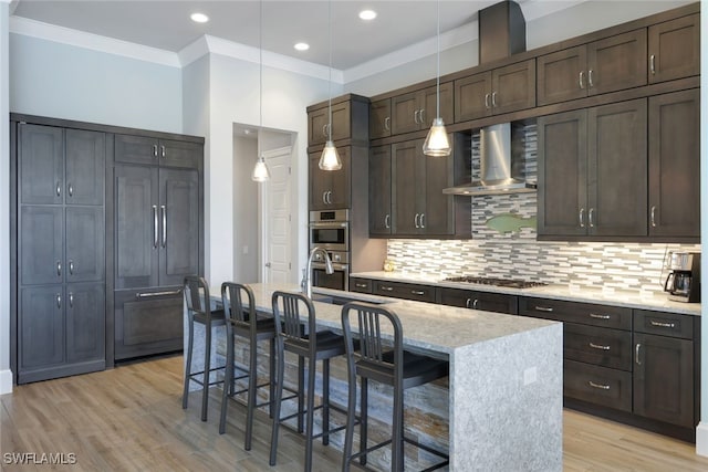 kitchen with a center island with sink, a breakfast bar, wall chimney range hood, and stainless steel appliances