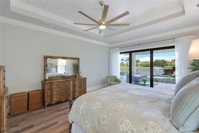 bedroom featuring a water view, wood finished floors, baseboards, access to outside, and a raised ceiling