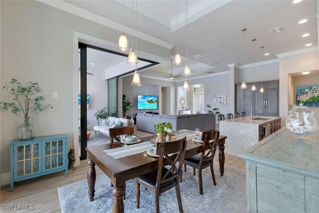 dining room featuring a tray ceiling, sink, light hardwood / wood-style floors, and ornamental molding