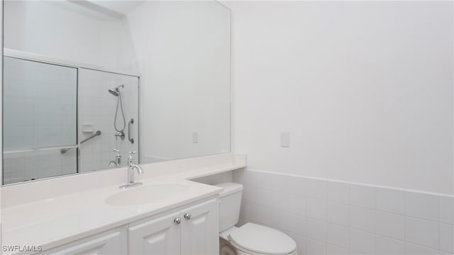 bathroom featuring a tile shower, vanity, tile walls, and toilet