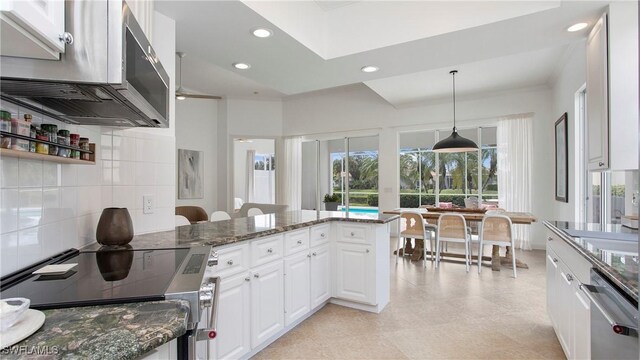 kitchen featuring white cabinets, range, decorative light fixtures, and dark stone counters