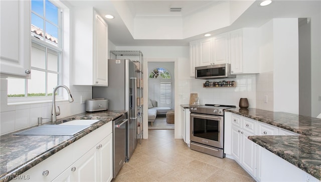 kitchen with white cabinets, appliances with stainless steel finishes, dark stone countertops, and sink