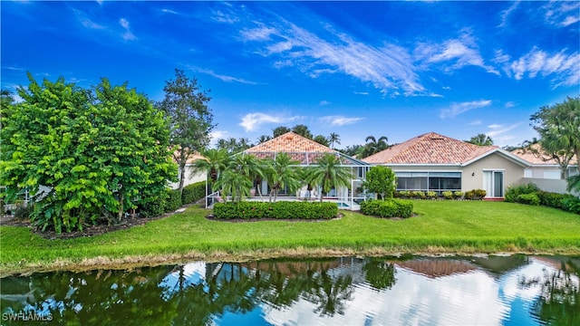 rear view of house featuring a lanai, a lawn, and a water view