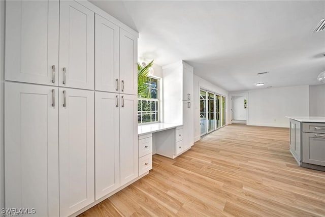 kitchen with built in desk, light hardwood / wood-style floors, and white cabinets