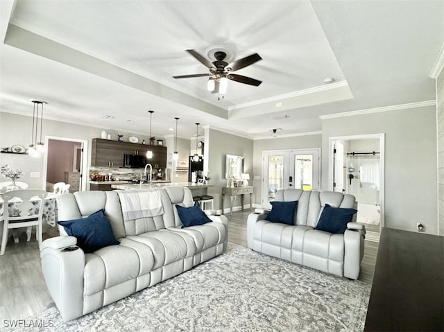 living room with crown molding, a tray ceiling, ceiling fan, and light hardwood / wood-style flooring