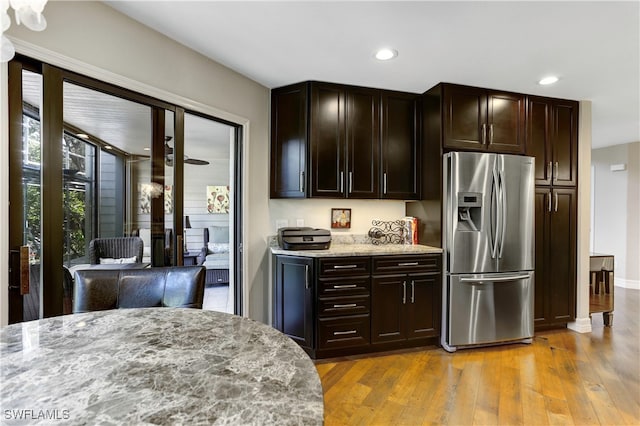 kitchen with light stone countertops, dark brown cabinets, stainless steel refrigerator with ice dispenser, and light hardwood / wood-style floors