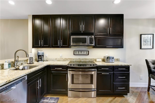 kitchen with light wood-type flooring, sink, dark brown cabinets, stainless steel appliances, and light stone countertops