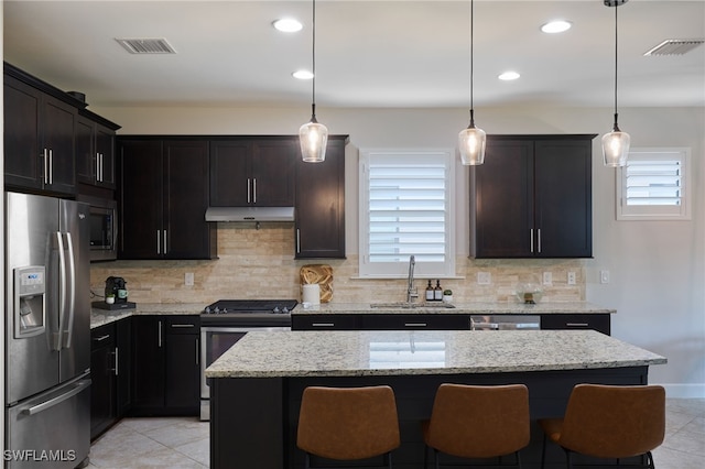 kitchen featuring appliances with stainless steel finishes, sink, hanging light fixtures, a center island, and light stone counters