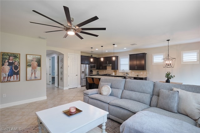 tiled living room with ceiling fan with notable chandelier, plenty of natural light, and sink