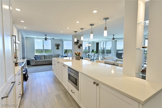 kitchen featuring ceiling fan, white cabinets, light stone counters, decorative light fixtures, and stainless steel microwave