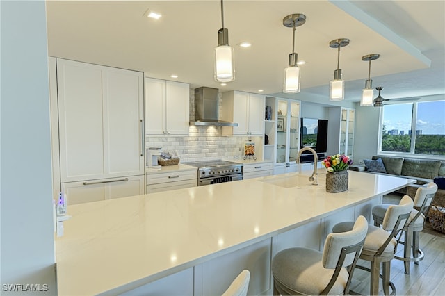 kitchen featuring pendant lighting, sink, white cabinets, wall chimney range hood, and light hardwood / wood-style flooring