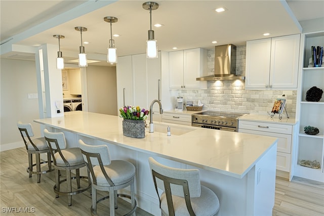 kitchen featuring white cabinets, wall chimney exhaust hood, high end range, decorative light fixtures, and washing machine and dryer