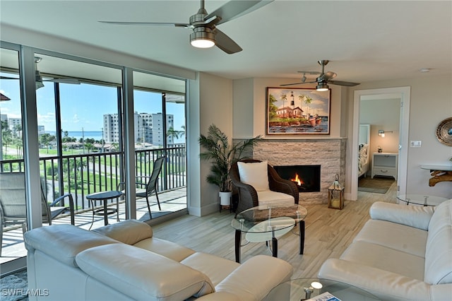 living room with ceiling fan, a stone fireplace, and light wood-type flooring