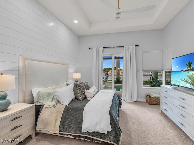 bedroom with a raised ceiling, ceiling fan, light colored carpet, and access to exterior