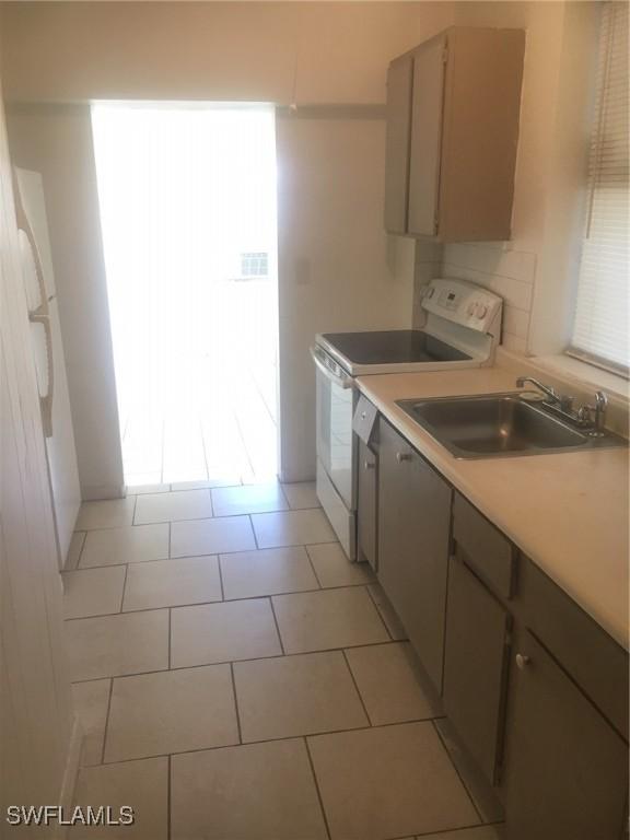 kitchen featuring decorative backsplash, light tile patterned flooring, sink, and electric range