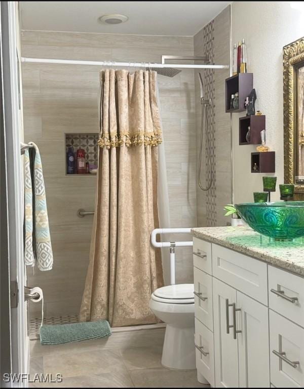 bathroom featuring tile patterned flooring, toilet, vanity, and a tile shower