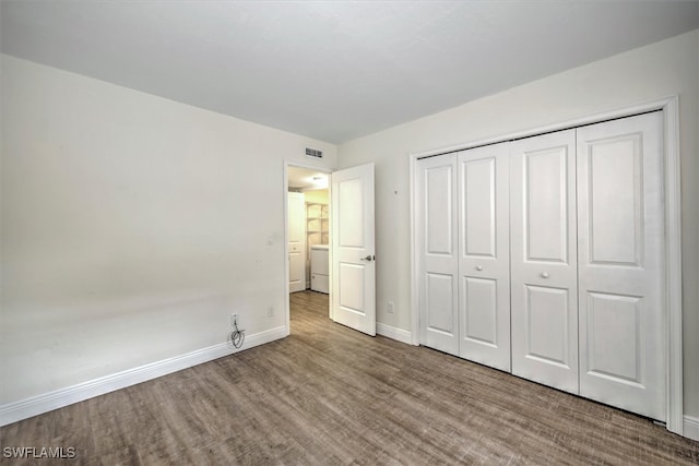 unfurnished bedroom with washer / clothes dryer, hardwood / wood-style flooring, and a closet