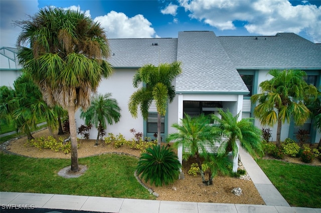 view of front of property featuring a shingled roof, a front lawn, and stucco siding