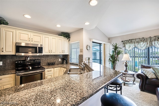 kitchen featuring a peninsula, a breakfast bar, a sink, appliances with stainless steel finishes, and dark stone counters