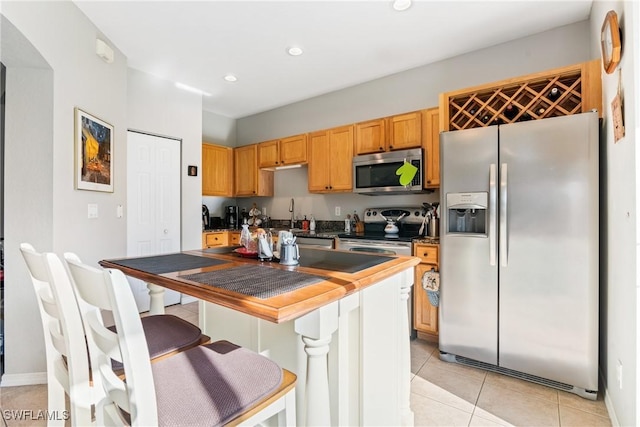 kitchen featuring a breakfast bar area, recessed lighting, light tile patterned floors, stainless steel appliances, and dark countertops