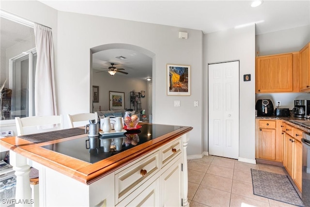 kitchen with light tile patterned floors, baseboards, dark countertops, arched walkways, and ceiling fan