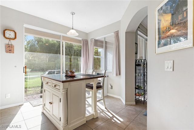 kitchen with a kitchen island, decorative light fixtures, white cabinets, a kitchen bar, and light tile patterned floors